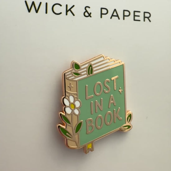 Book-themed enamel pin reading “Lost in a Book,” by Wick and Paper.